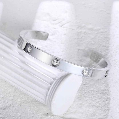 Silver love cuff bracelet resting on white column, showcasing its minimalist waterproof design with sparkling zirconia accents.