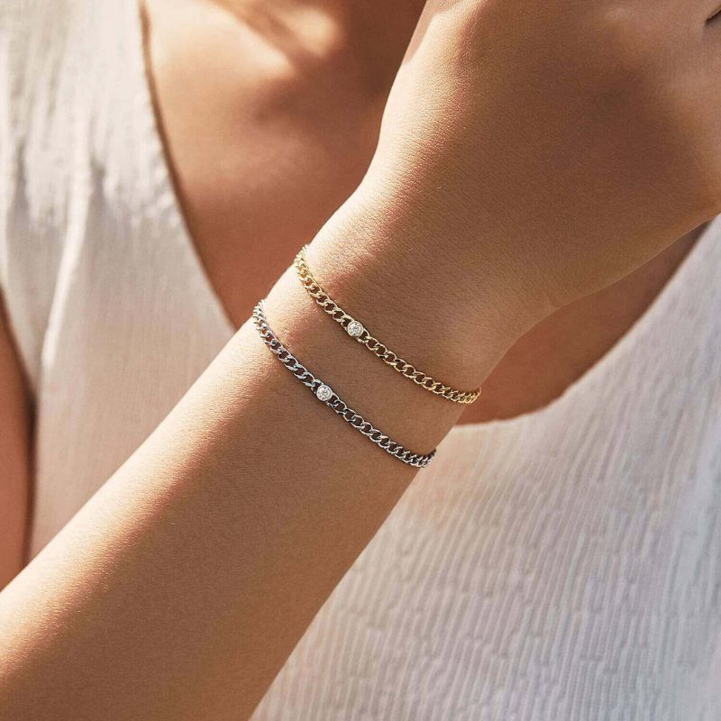 Close-up of a person's wrist wearing two gold bracelets on a neutral background